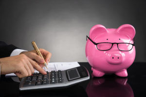 Close-up of businessperson with piggybank calculating tax at desk