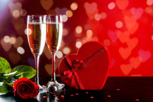 Background of Valentine's Day celebration with champagne, rose, heart-shaped present and red candies.