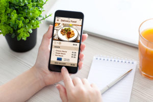 Women hand holding phone with app delivery food on screen above desk
