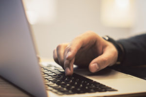 Side view of man hands using notebook keyboard on wooden desk top workplace