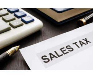 A calculator next to a pen next to a paper stating, 'Sales Tax' on a desk. 