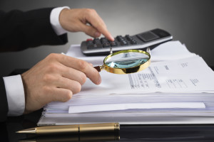 This is a picture of a person looking at papers with a magnifying glass and calculator. 